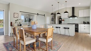 A modern kitchen with a wooden dining table, white cabinets, and pendant lighting. - Meadow Escape - Mangawhai Holiday Home (Mangawhai)