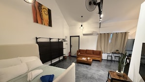 Una habitación de hotel moderna con cama, sofá, una mesita, un ventilador y un cuadro en la pared.
