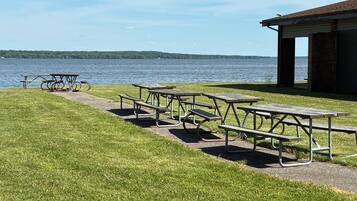 A grassy area with picnic tables and a building with a roof, near a body of water.