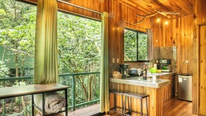Una cabaña de madera con cocina, comedor con mesa y sillas, y vista al bosque circundante.