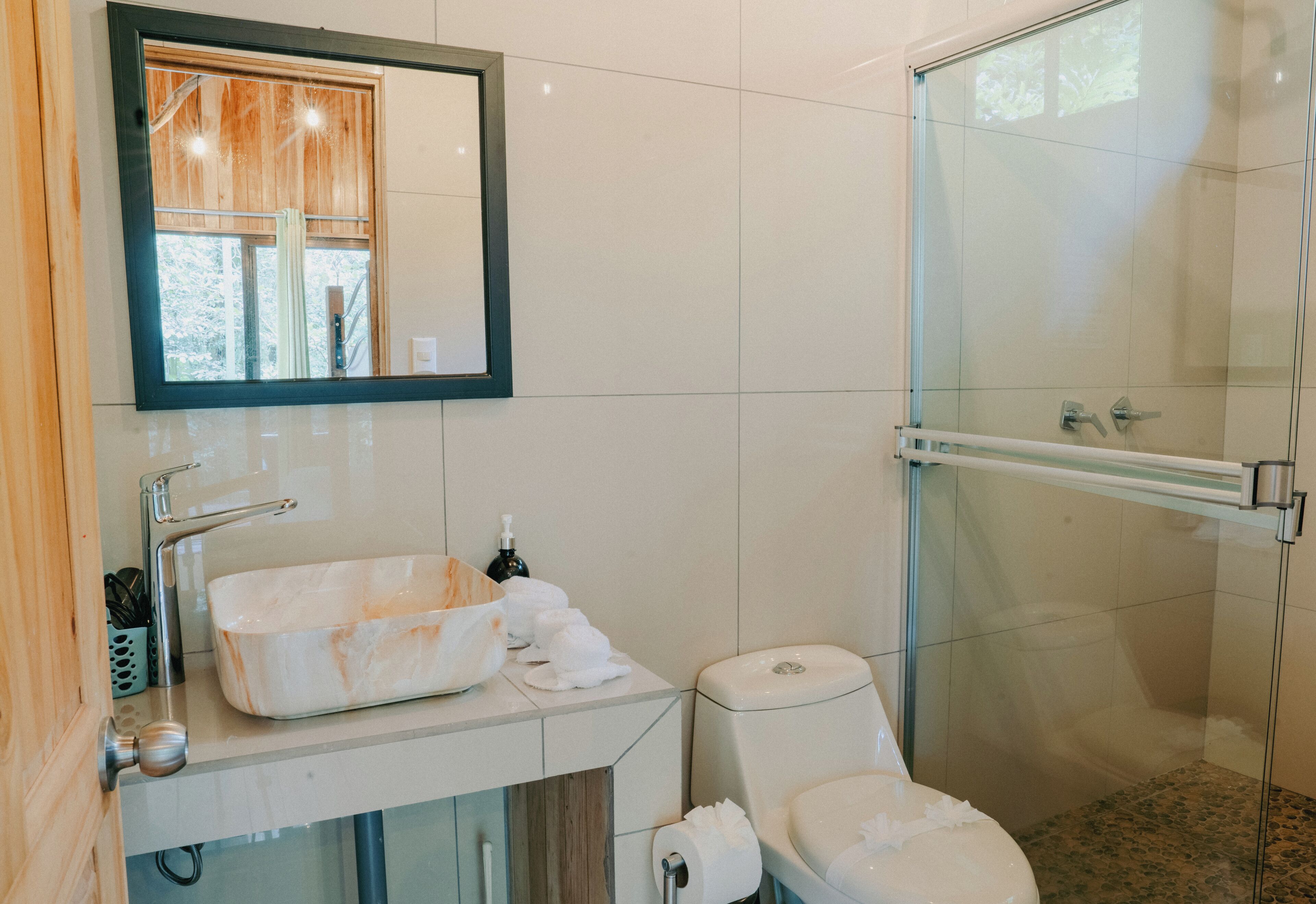Un baño con cabina de ducha de vidrio, un lavabo blanco con lavamanos de mármol y un inodoro.