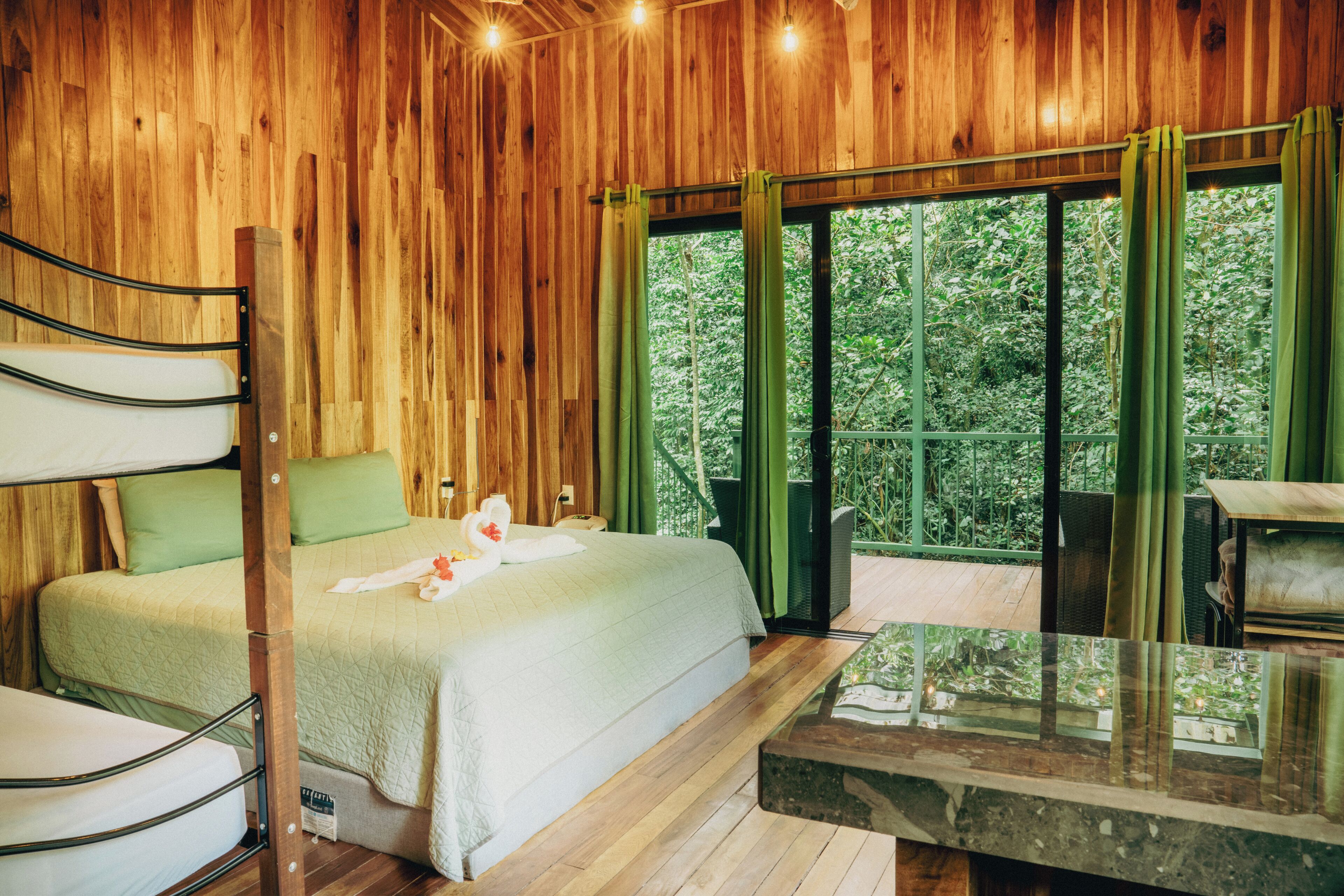 A wooden room with a bed, bunk beds, and a glass table.