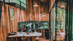 Interior de madera con una mesa de comedor para cuatro, zona de cocina y vista a través de un ventanal.