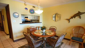 Un coin repas avec une table ronde, des chaises en osier, un lustre et une décoration représentant un poisson au mur.