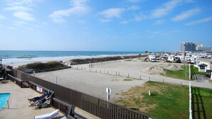 Une plage avec vue sur une piscine, des chaises longues et des véhicules récréatifs.