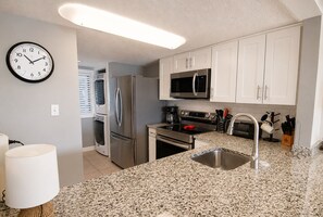 A modern kitchen with stainless steel appliances, a granite countertop, and white cabinetry. - Land's End Resort - Oceanfront Views & Resort Amenities (Myrtle Beach)