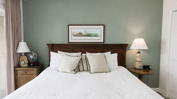 A neatly made bed with white linens, a wooden headboard, and a framed picture above it. - Land's End Resort - Oceanfront Views & Resort Amenities (Myrtle Beach)