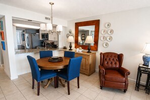 A dining area with a round table, blue chairs, a brown leather chair, a wooden cabinet, and a mirror on the wall. - Land's End Resort - Oceanfront Views & Resort Amenities (Myrtle Beach)