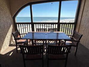 A covered outdoor seating area with a table and chairs, overlooking a beach. - Land's End Resort - Family Retreat with Ocean Views, Pools & Spacious Layout (Myrtle Beach)