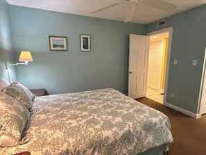 A bedroom with a bed, a nightstand, a lamp, and two framed pictures on the wall. - Land's End Resort - Family Retreat with Ocean Views, Pools & Spacious Layout (Myrtle Beach)