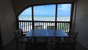 Ein Zimmer mit großem Fenster mit Blick auf einen Strand, einem Deckenventilator und einem Tisch mit Stühlen.