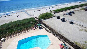 Zona de piscina con vista a la playa, un muelle cercado y un puesto de salvavidas.