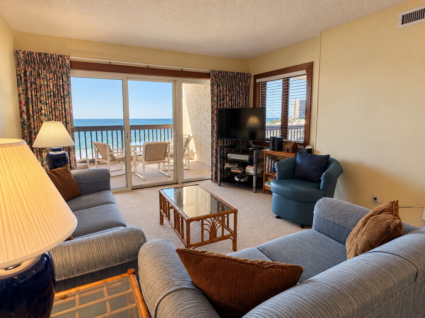 Ein Wohnzimmer mit einer Couch, Sesseln, einem Couchtisch, einem Fernseher und einem Balkon mit Meerblick.