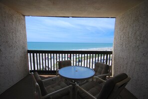 Ein Balkon mit Blick auf den Strand, einem runden Tisch und vier Stühlen.