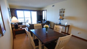 Un comedor con una mesa, sillas, un jarrón con flores, una lámpara y un televisor al fondo.