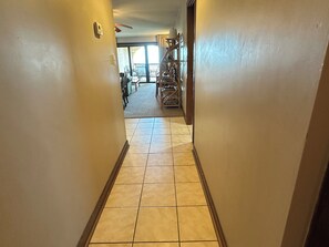 A hallway with a tiled floor leading to a room with a ceiling fan and a view of a balcony. - Land's End Resort - Beachfront 2BR Escape with Ocean Views & Resort-Style Amenit (Myrtle Beach)