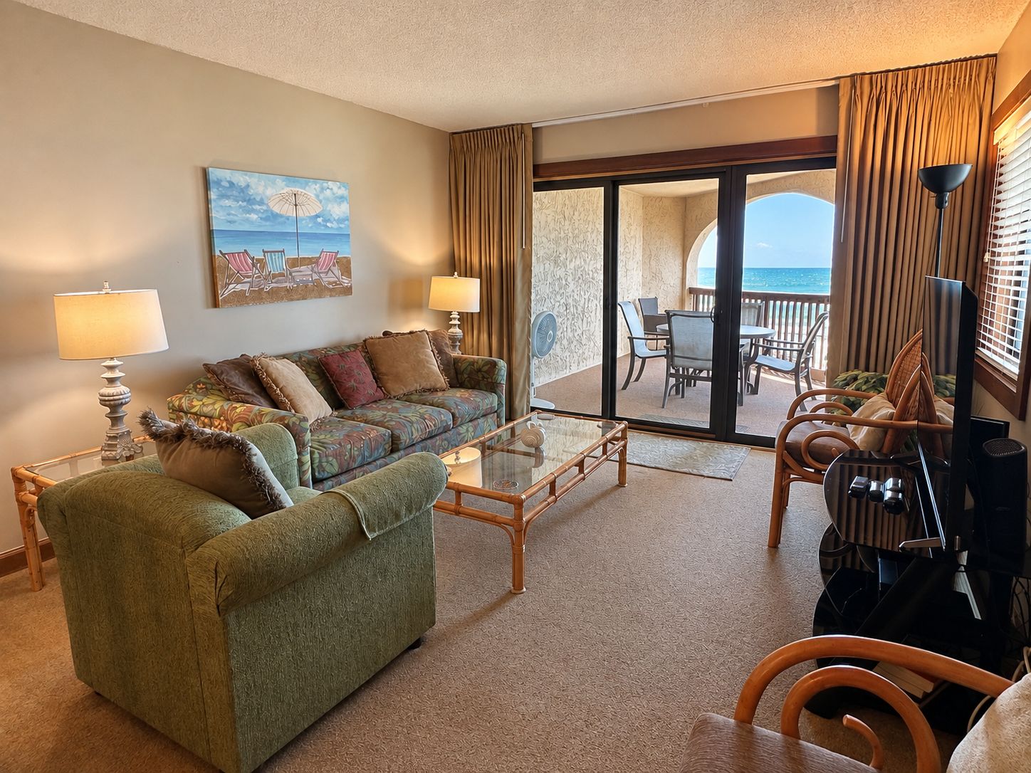 A hotel room with a sofa, armchairs, a glass coffee table, and a view of the ocean through a sliding door.
