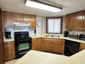 A kitchen with wooden cabinets, a stove, a dishwasher, a sink, and a clock on the wall. - Land's End Resort - Beachfront 2BR Escape with Ocean Views & Resort-Style Amenit (Myrtle Beach)