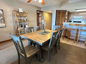 A dining area with a wooden table and chairs, a kitchen with wooden cabinets, and a ceiling fan. - Land's End Resort - Beachfront 2BR Escape with Ocean Views & Resort-Style Amenit (Myrtle Beach)