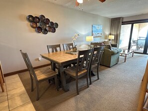 A dining area with a wooden table and chairs, a sofa, a lamp, and a wall art piece. - Land's End Resort - Beachfront 2BR Escape with Ocean Views & Resort-Style Amenit (Myrtle Beach)
