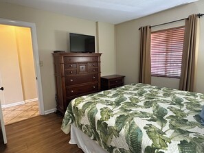A bedroom with a bed, a dresser, a television on top of the dresser, and a window with blinds. - Ocean View | King Suite, Balcony & Beach Access (Myrtle Beach)