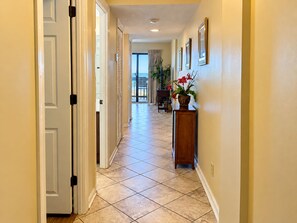 A hallway with a tiled floor, a wooden console table with a potted plant, and a door with a black handle. - Ocean View | King Suite, Balcony & Beach Access (Myrtle Beach)
