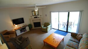 Ein Wohnzimmer mit Fernseher, Sofa, Couchtisch, Kamin und einer Glastür, die auf eine Terrasse im Freien führt.
