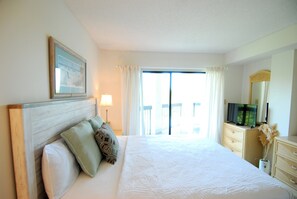 A hotel room with a bed, a television, a dresser, and a window with curtains. - Land's End Resort | 3BR Ocean View Condo Near Beach & Attractions (Myrtle Beach)