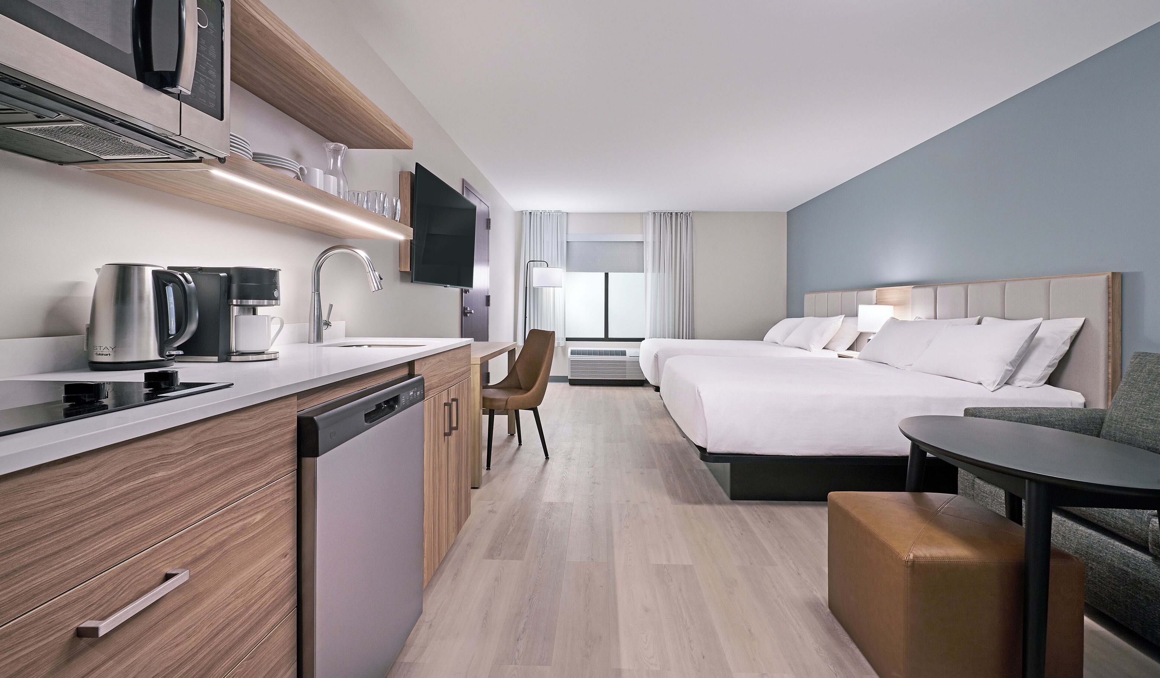 Ein modernes Hotelzimmer mit einer Küchenzeile, einem Bett, einem Schreibtisch und einer Sitzecke.