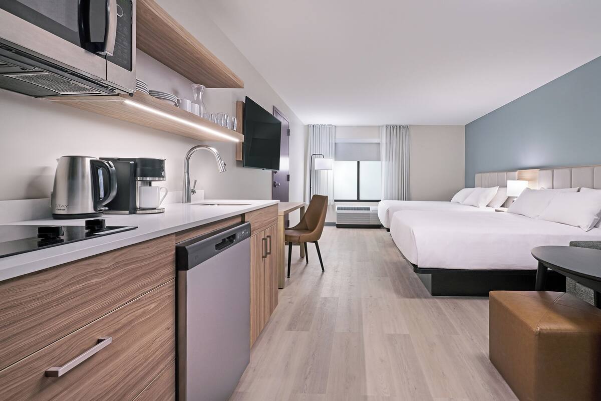 Quarto de hotel moderno com cozinha compacta, cama, escrivaninha e área de estar.