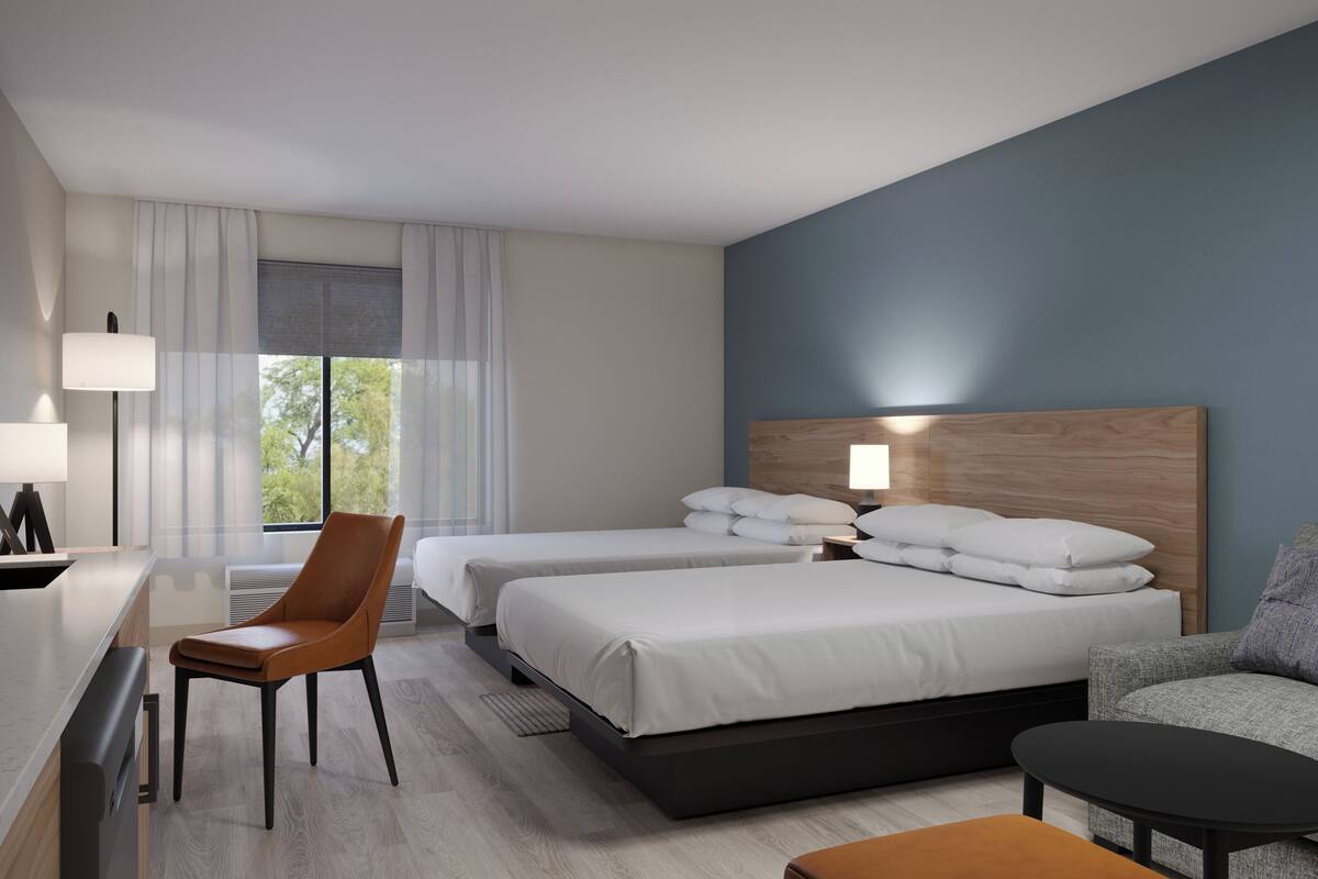 Quarto de hotel com duas camas, uma escrivaninha, uma cadeira, um sofá e uma mesa de centro.