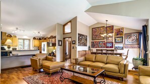 A spacious living room with a large sofa, a coffee table, and a dining area with a chandelier. - Garden Trails! Spacious Home by Garden of the Gods (Colorado Springs)
