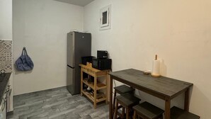 Une petite cuisine équipée d’un réfrigérateur, d’un four à micro-ondes, d’une table en bois avec des tabourets et d’un sac suspendu.