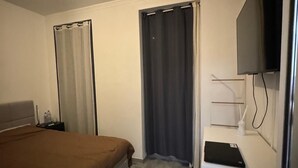 Une chambre d’hôtel avec un lit, un bureau, une télévision et un rideau de douche.