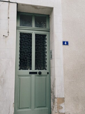 Une porte verte avec une fenêtre, une plaque portant le numéro « 4 », et un mur à la texture particulière.