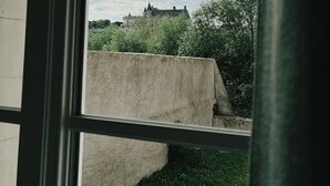 En vy genom ett fönster i en byggnad med en stor betongkonstruktion och en avlägsen byggnad som liknar ett slott.