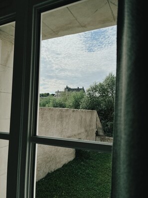 Une vue à travers la fenêtre d’un bâtiment doté d’une grande structure en béton et d  ’un autre bâtiment, plus éloigné, qui ressemble à un château.