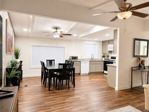 A modern kitchen with a dining area, wooden flooring, ceiling fans, and a large window. - River Retreat Near Needles-Sleeps 8-Boat Parking-Fully Furnished-Snowbirds (Mohave Valley)