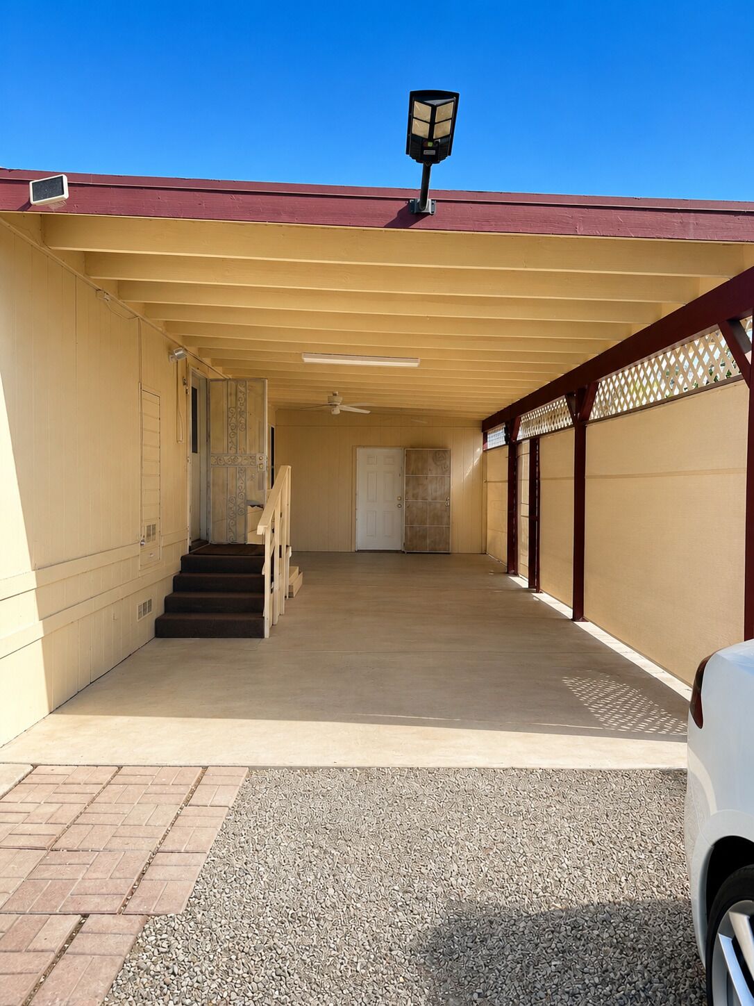 A covered parking area with a staircase leading to a door, a ceiling fan, and a security light.