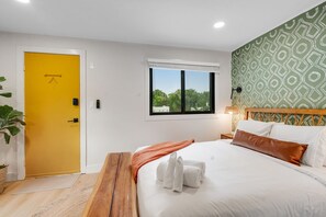 Ein Hotelzimmer mit gelber Tür, einem Bett mit weißen Leinen, einer braunen Tagesdecke und einer Wand mit grünem Muster.