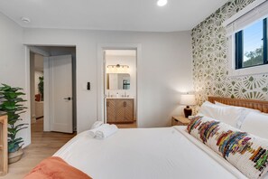 Ein Hotelzimmer mit einem Bett, einem Nachttisch, einer Lampe, einem Fenster, einem Badezimmer mit Spiegel und einer Tür.