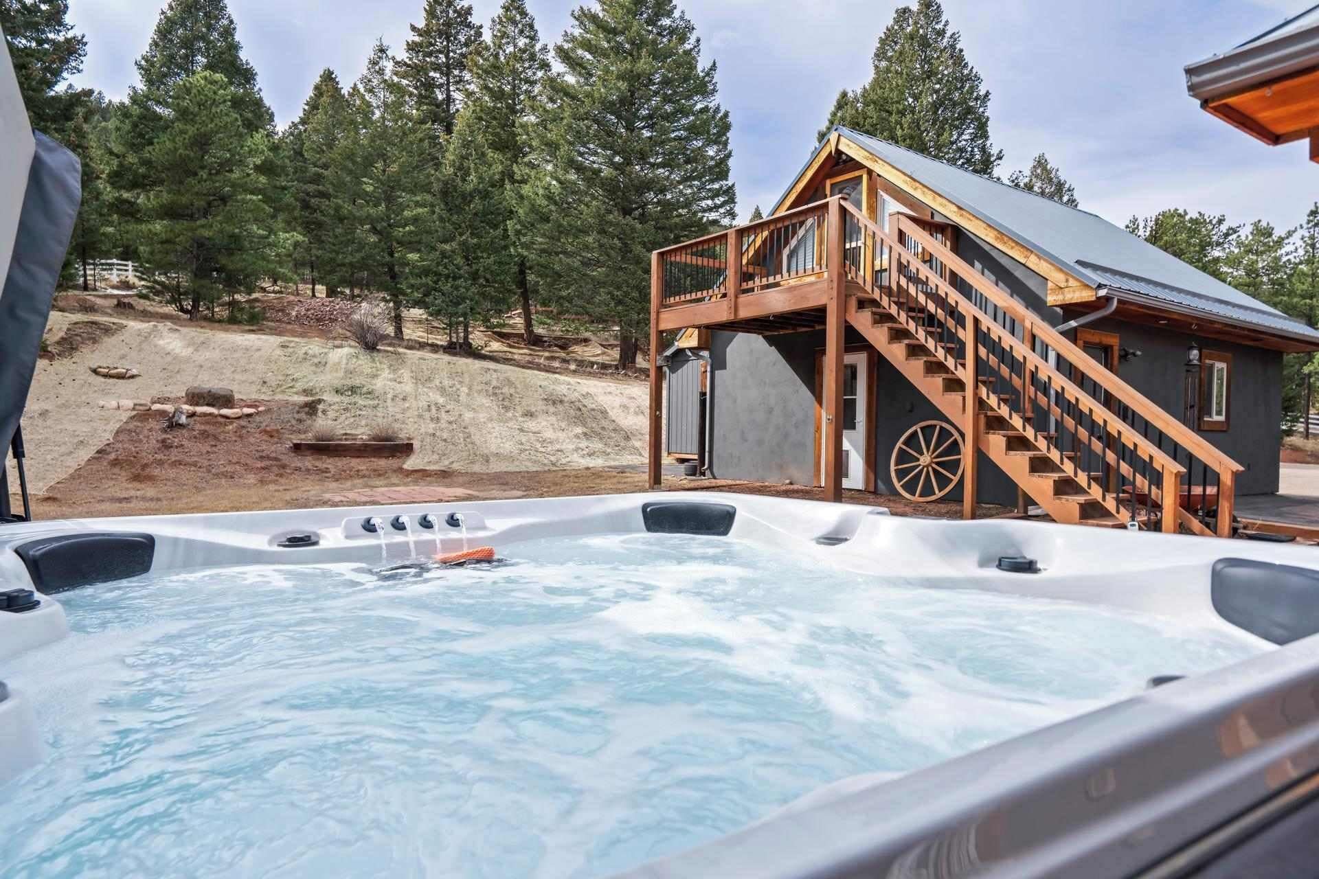 Un bain à remous avec une terrasse en bois et des escaliers menant à un chalet situé dans une zone boisée.