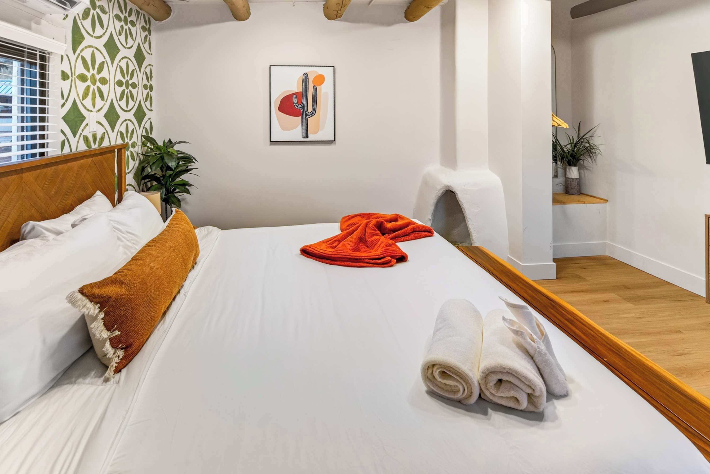 A hotel room with a bed, a chair, a plant, and a painting on the wall.