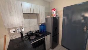 Uma cozinha compacta com fogão, panelas, um dispensador de água azul e uma geladeira.