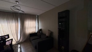 Uma sala de estar com sofá, um rack para TV e uma janela com cortinas.