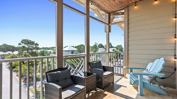 A balcony with wicker furniture and a blue Adirondack chair, overlooking a residential area. - Seagrove Highlands Unit 1410 (Santa Rosa Beach)