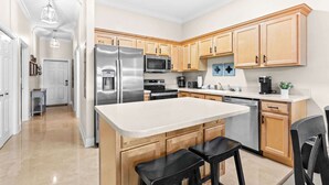 A modern kitchen with wooden cabinets, stainless steel appliances, and a central island with seating. - Seagrove Highlands Unit 1410 (Santa Rosa Beach)