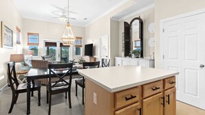A spacious kitchen with a large island, dining area with chairs, a ceiling fan, and a view of the outdoors. - Seagrove Highlands Unit 1410 (Santa Rosa Beach)