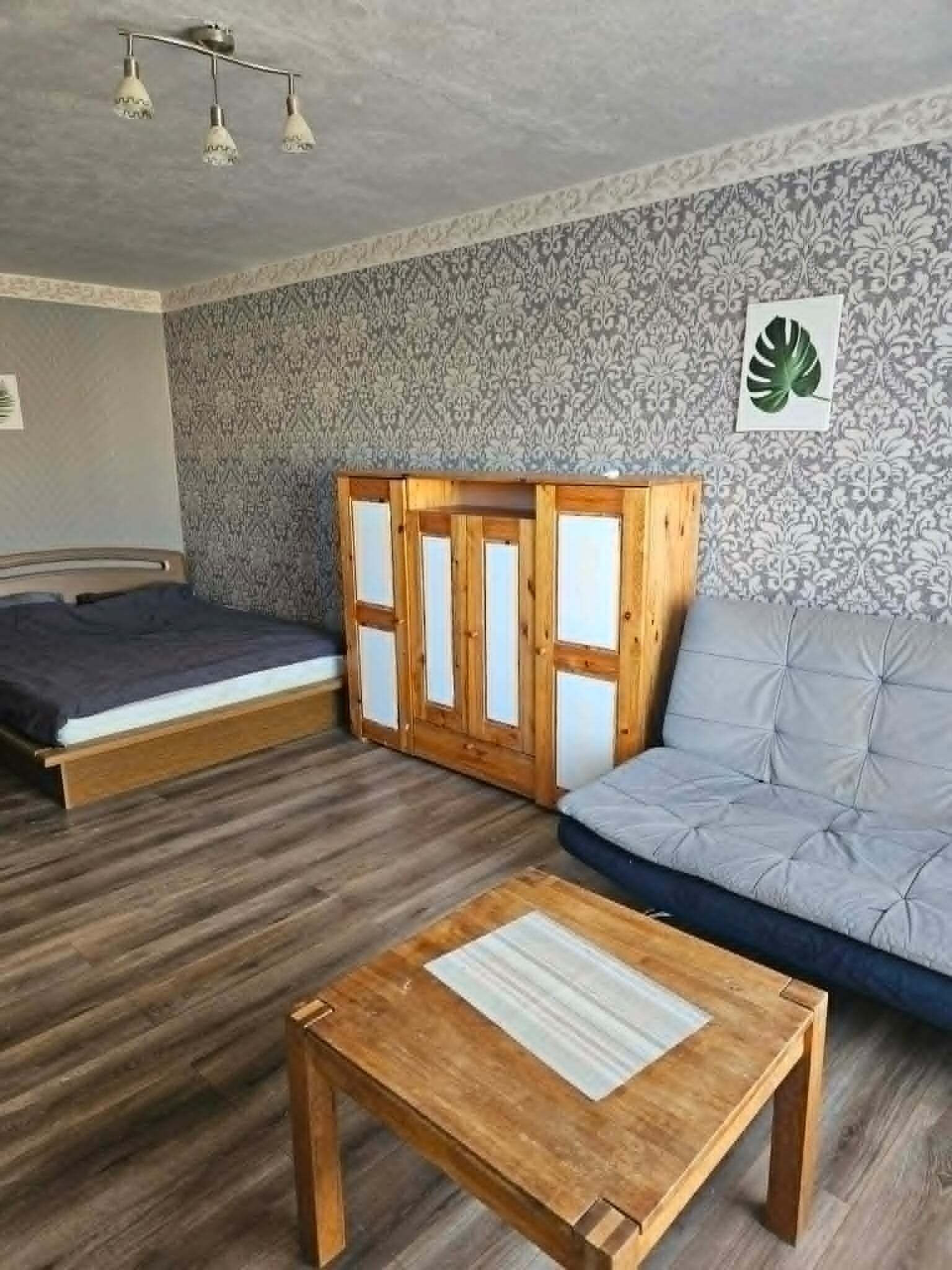 Ein Zimmer mit einem Bett, einem Schlafsofa, einem Holztisch und einer Wand mit Muster.