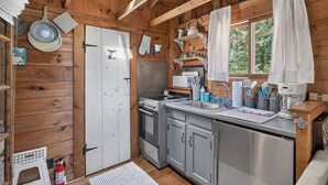 Cocina compacta con paredes de madera, un lavamanos de acero inoxidable y una ventana con cortinas.